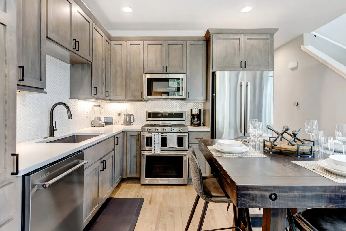 A chef’s kitchen with modern appliances, warm wood cabinetry, and a dining table ready for a gathering. The kitchen is stocked for culinary creativity, while the adjacent dining area is prepared for friends and family to enjoy meals together.