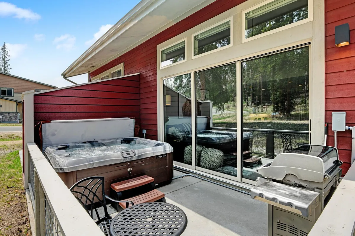 A scenic view of the private patio featuring the brand new hot tub, inviting outdoor seating, and a grill. The natural surroundings hint at the fresh mountain air and year-round enjoyment, from tranquil mornings to lively evenings with friends.