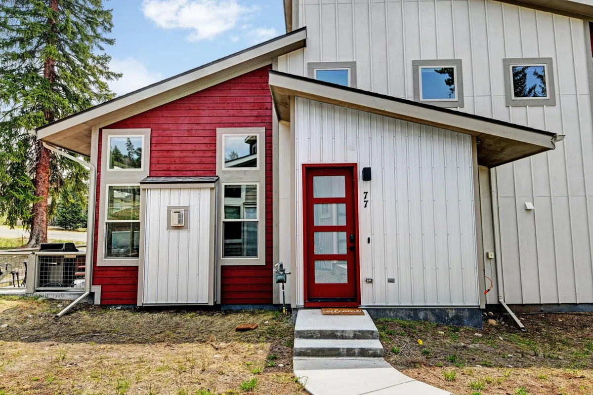 This image showcases the home's exterior with a welcoming red accent wall, large windows, and a front door featuring window panels. The inviting porch area is surrounded by trees, providing a sense of outdoor space and connection to nature.