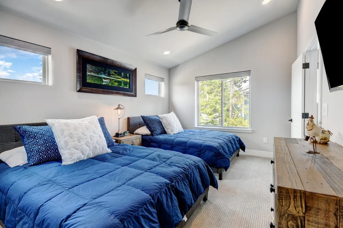 A cozy bedroom featuring two twin beds, each dressed in soft linens and set against a backdrop of decorative artwork. A window lets in natural light, enhancing the room's calm and inviting mood.