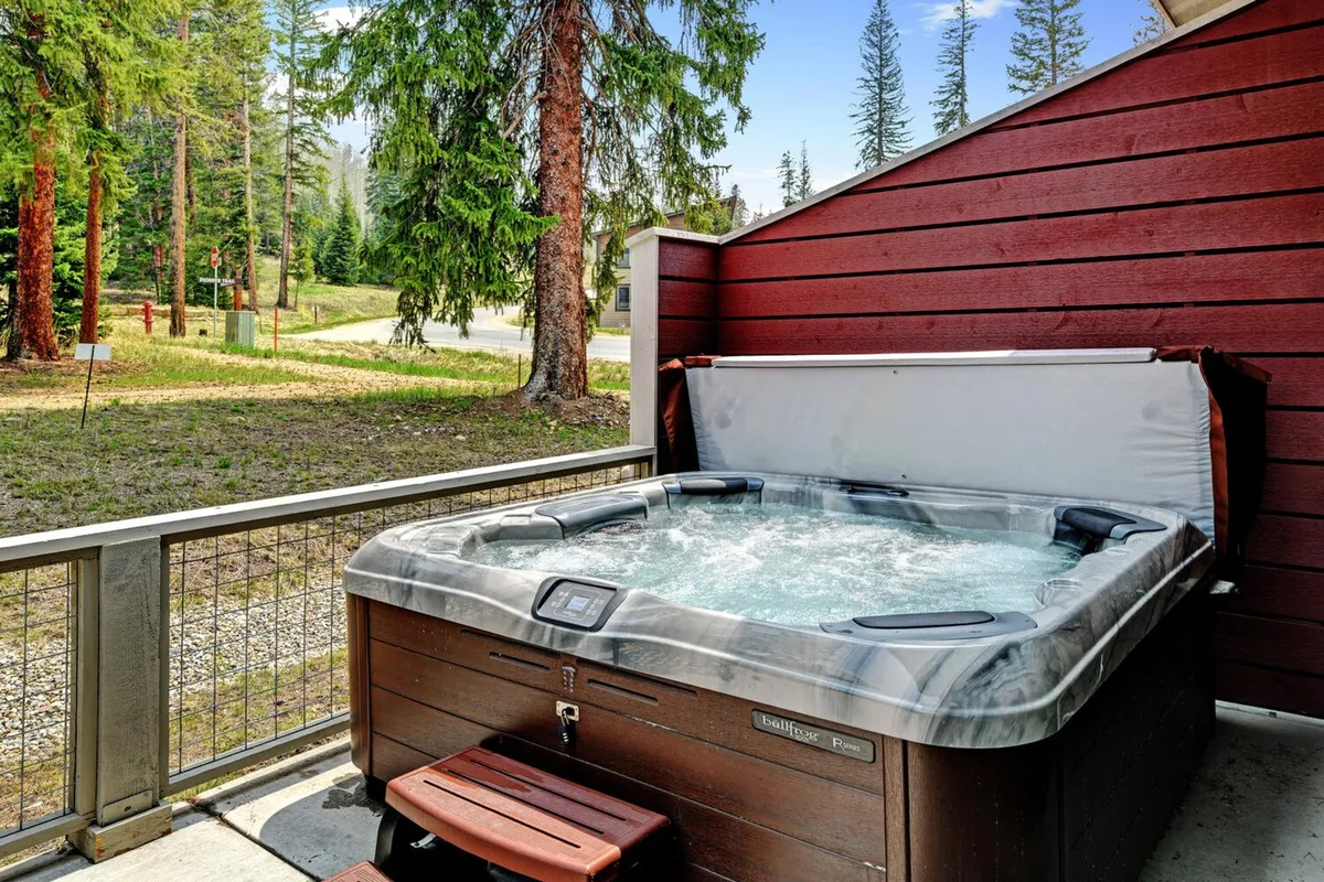 An exterior view of a private hot tub nestled among tall trees, with a fenced area providing privacy and a peaceful natural setting. The scene suggests relaxation after a day of adventure, underlining the transition from outdoor thrills to ultimate comfort.