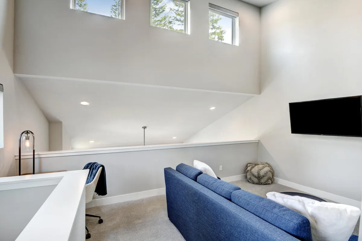 A bright, airy living room with a blue sofa positioned to enjoy both a flat-screen TV and expansive windows that offer views to the outdoors. The room feels welcoming and open, inviting both relaxation and connection to the landscape beyond.