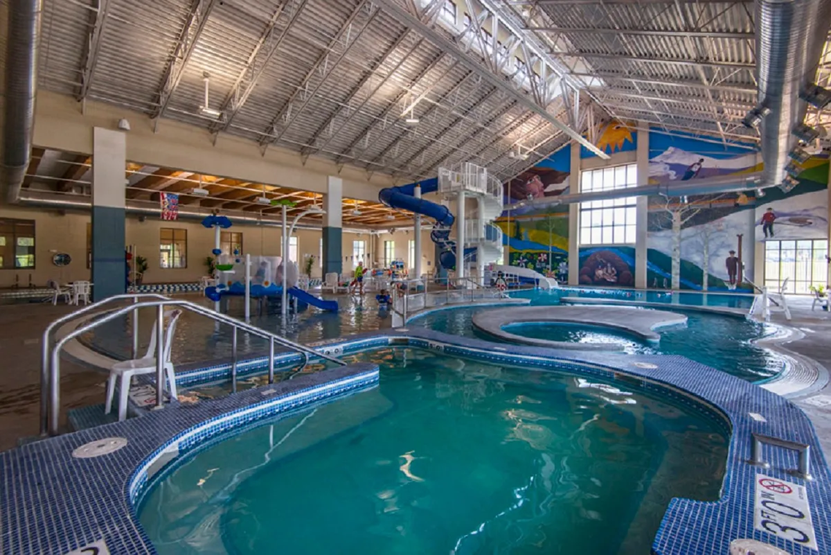 A lively interior shot of the Grand Park Rec Center, showing water slides, swimming pools, and children playing amid colorful murals. The scene bursts with energy and captures a quintessential family-friendly indoor activity.