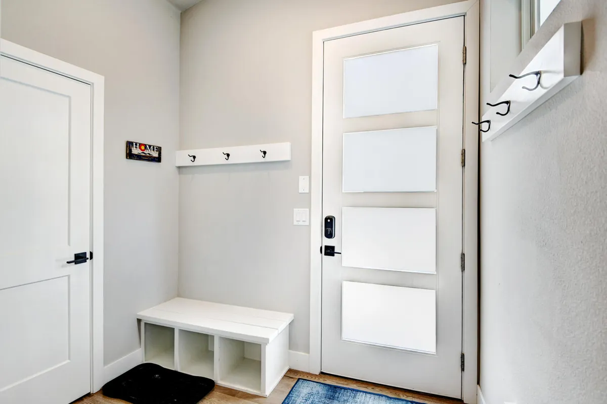 A cozy entryway features a welcoming front door, a bench for removing shoes, and convenient coat hooks. The space is inviting, practical, and hints at family-friendly functionality—ideal for guests with children or pets needing a drop zone after outdoor adventures.