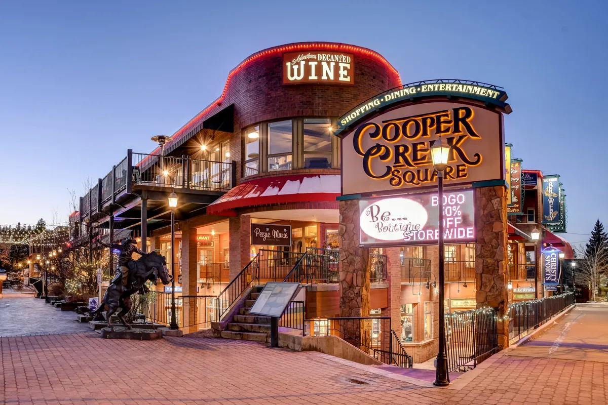 This image highlights the Cooper Creek Square sign, a wine shop sign, ornate architecture, a staircase, and a sculpture, creating an unmistakable sense of Winter Park's vibrant shopping and dining district. The scene bustles with the promise of entertainment and gatherings, inviting visitors to explore the local businesses and seasonal festivities.